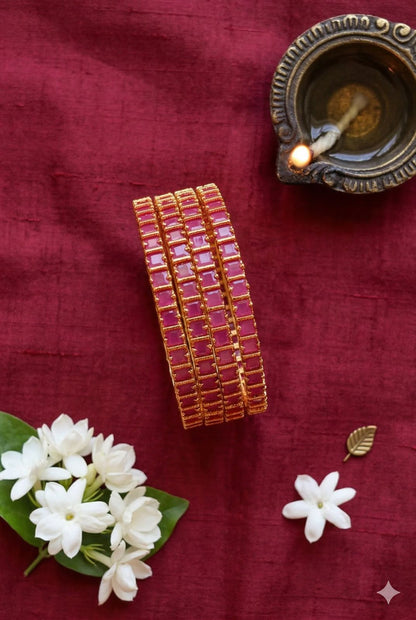 Set of gold bangles on a red fabric background with white flowers and a small lamp.